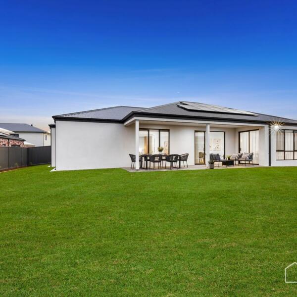 Rear exterior view showcasing landscaped backyard and alfresco area of a custom new home in Lara